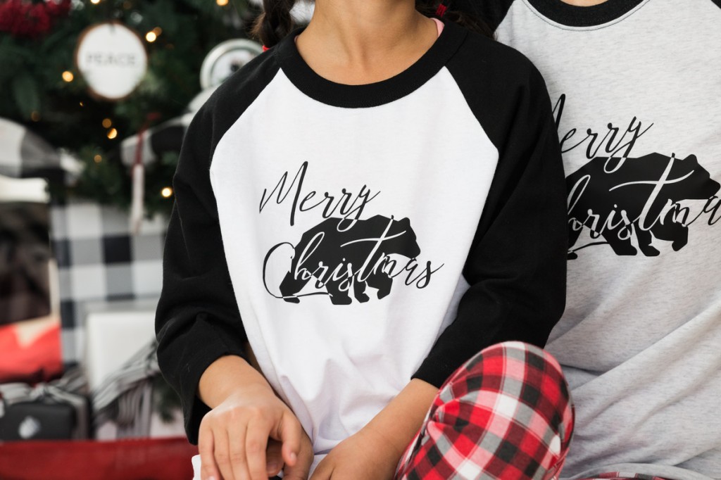 Merry Christmas printed with a bear in the background on a black and white t-shirt.